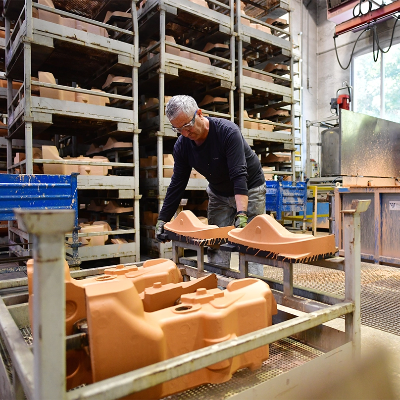 Ein Gießereimitarbeiter hantiert mit orangefarbenen Formteilen aus Sand für den Metallguss. Hinter ihm stehen Regale mit weiteren Formteilen.