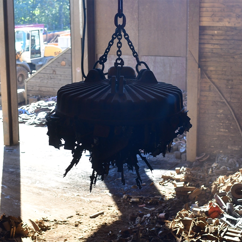 A lifting magnet picks up scrap metal at a recycling yard.