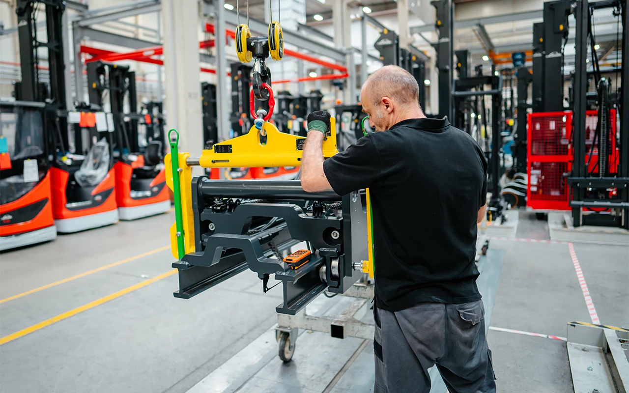 A worker uses a crane to position a heavy component in a production hall.